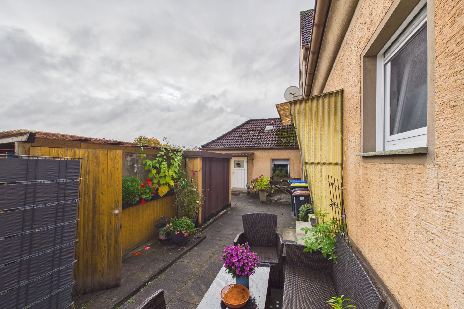 Kleiner Hinterhof mit Sitzgruppe, Pflanzen und angrenzender Hauswand.