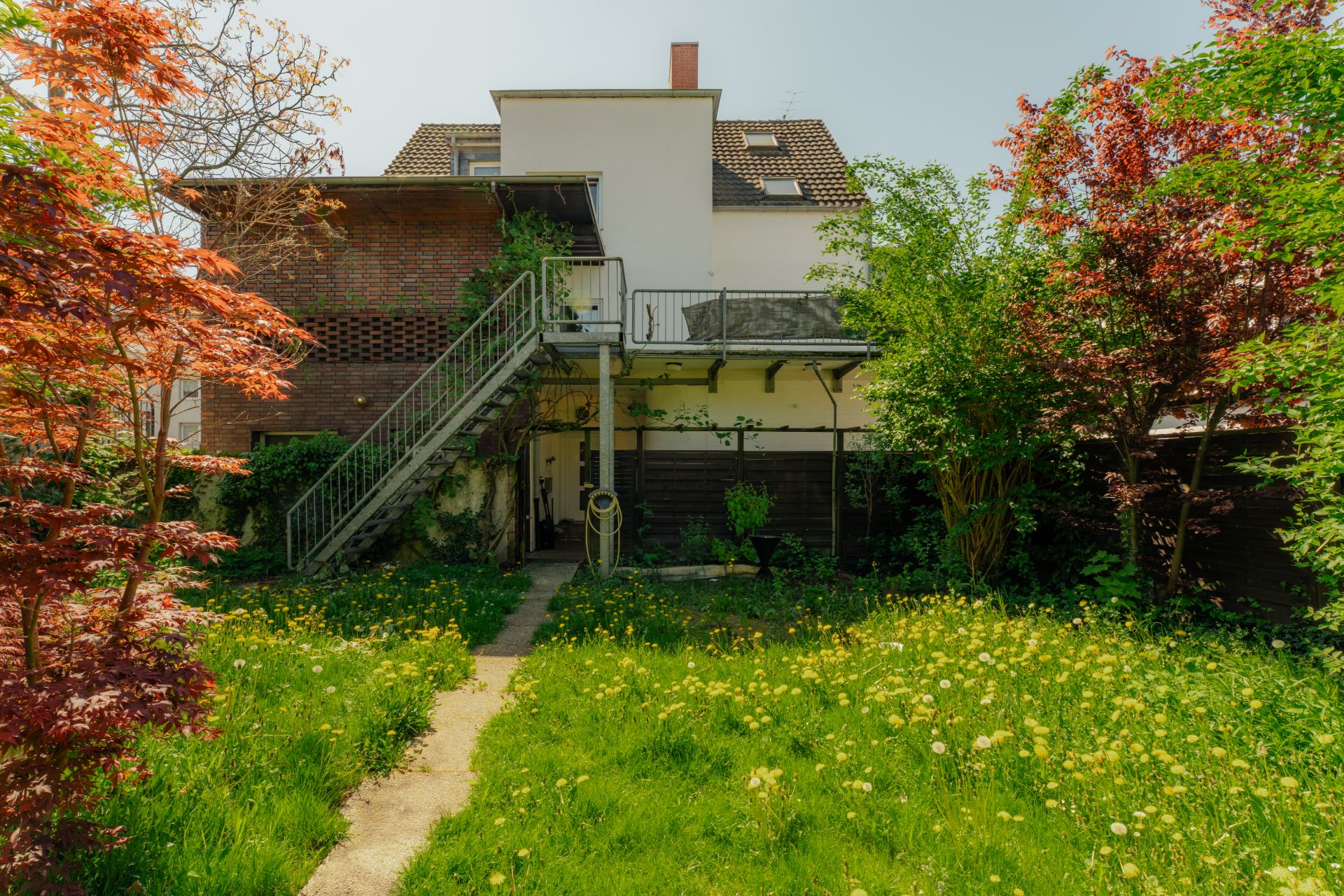 Wohnhaus mit Außentreppe und grünem Garten mit blühenden Bäumen und Wiese.