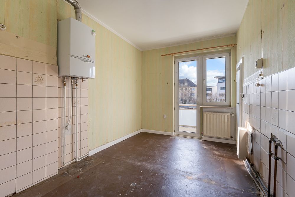 Leerer Raum mit Fliesen an den Wänden, Heizkörper und Gastherme, Fenster und Tür zum Balkon.