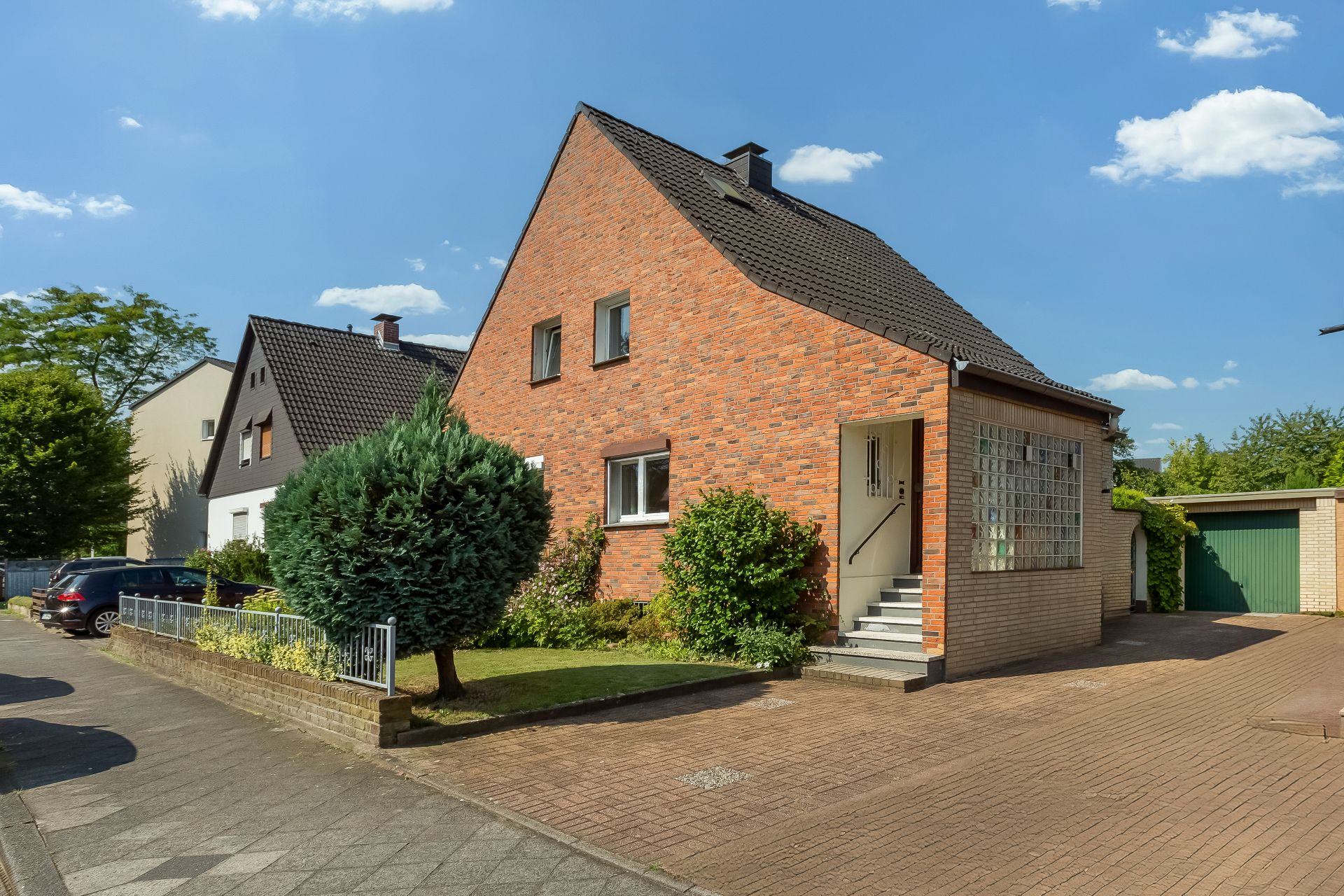 Backsteinhaus mit Satteldach, kleiner Garten und Garage, an einer ruhigen Straße gelegen.