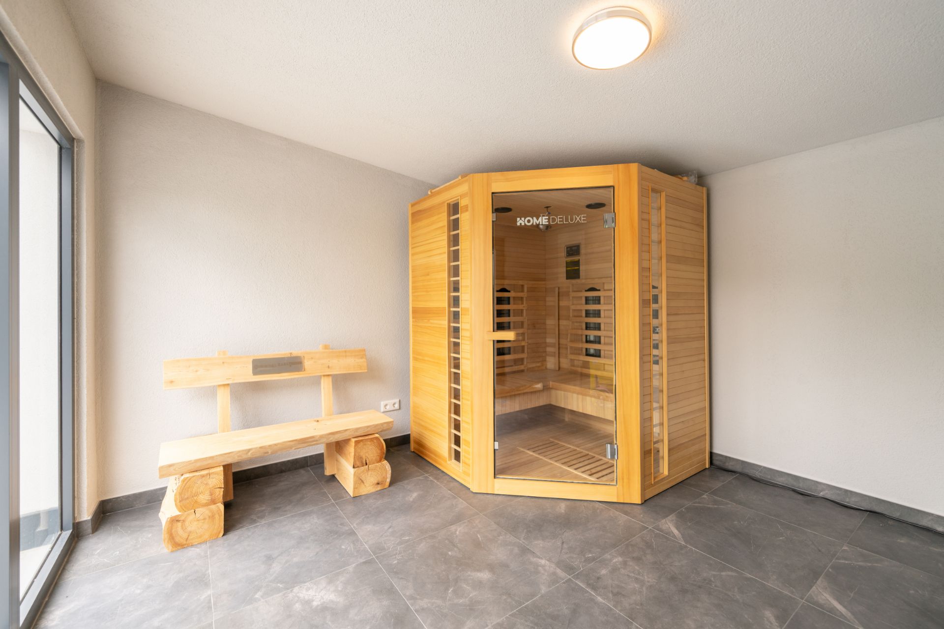 Holzsauna und Holzbank in einem hellen Raum mit Fliesenboden.