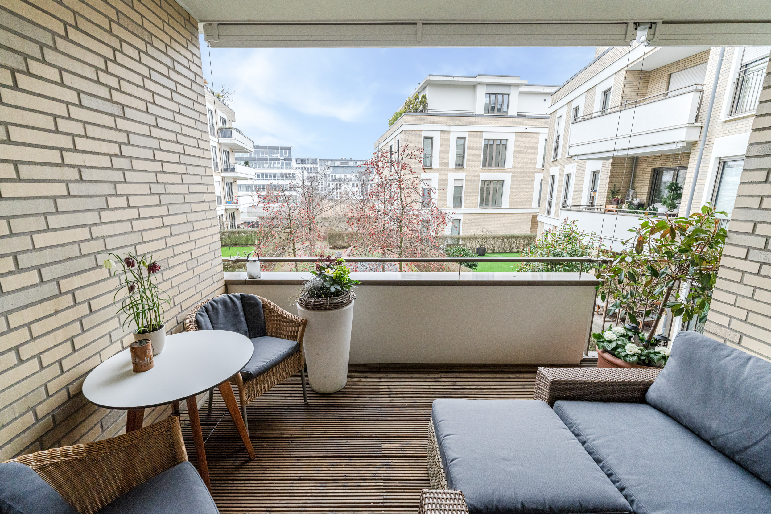 Balkon mit Sitzmöbeln, Tisch, Pflanzen und Blick auf moderne Wohngebäude.