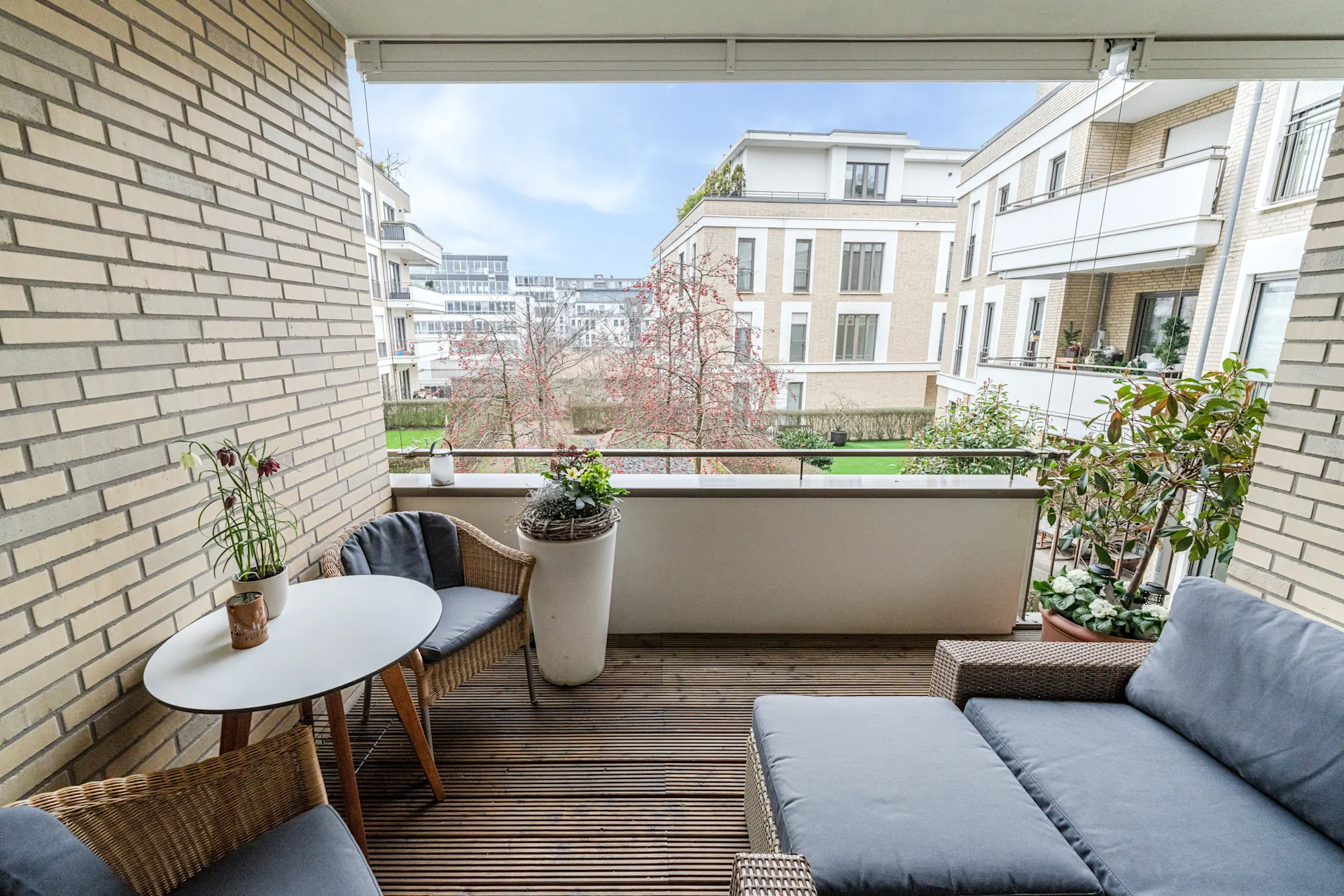 Balkon mit Sitzmöbeln, Tisch, Pflanzen und Blick auf moderne Wohngebäude.
