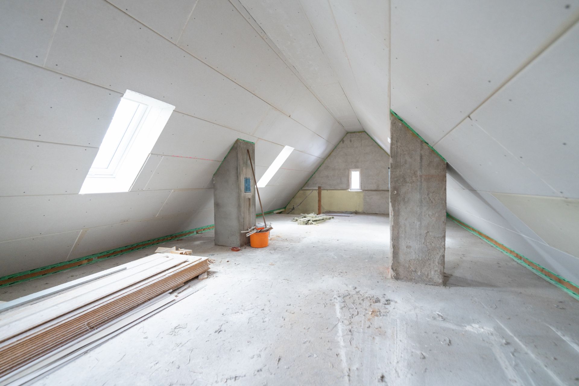 Ausgebauter Dachboden mit Schrägen, zwei Dachfenstern und Baumaterial am Boden.