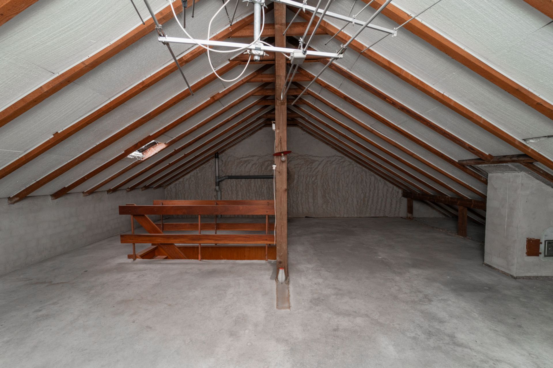 Leerer Dachboden mit sichtbaren Holzbalken und einem Holzregal in der Mitte.
