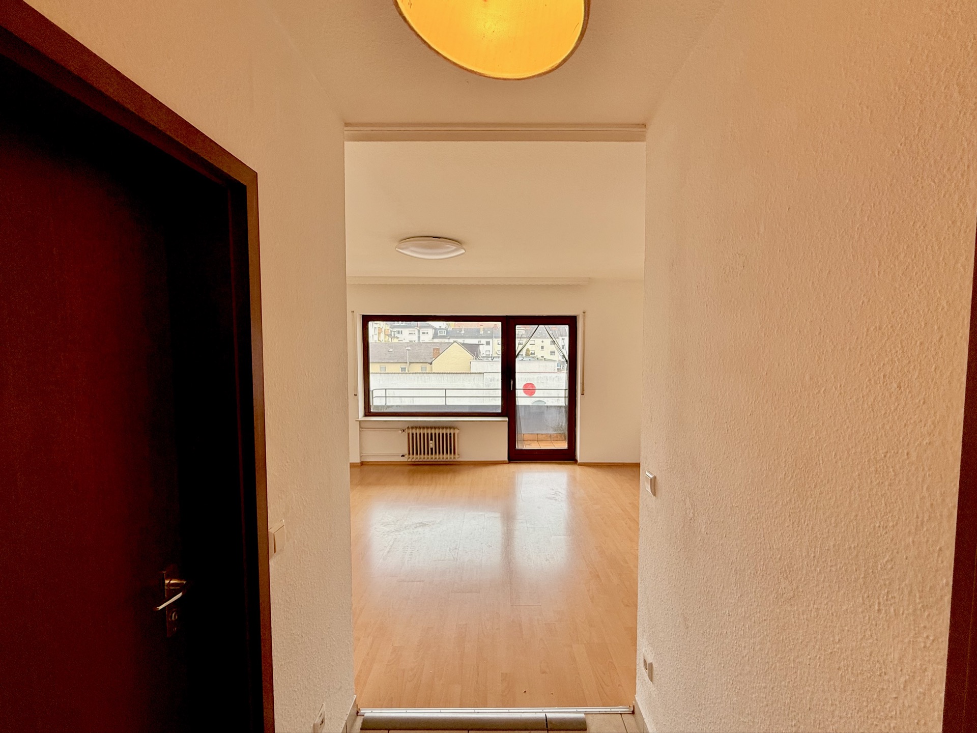 Blick vom Flur in ein helles Zimmer mit großem Fenster und Holzboden.