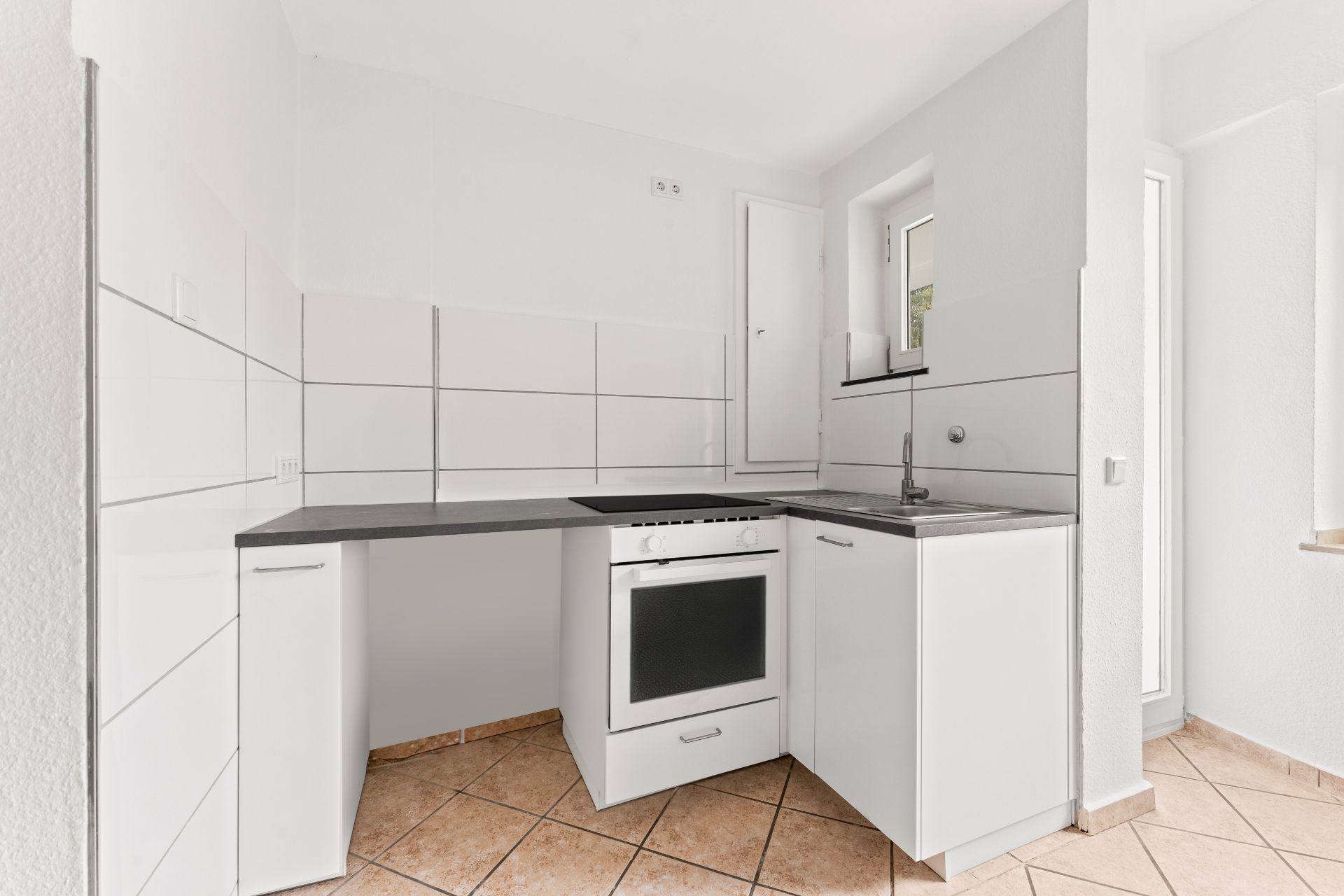 Helle Küche mit weißen Schränken, Backofen, Spüle und Fliesenboden.