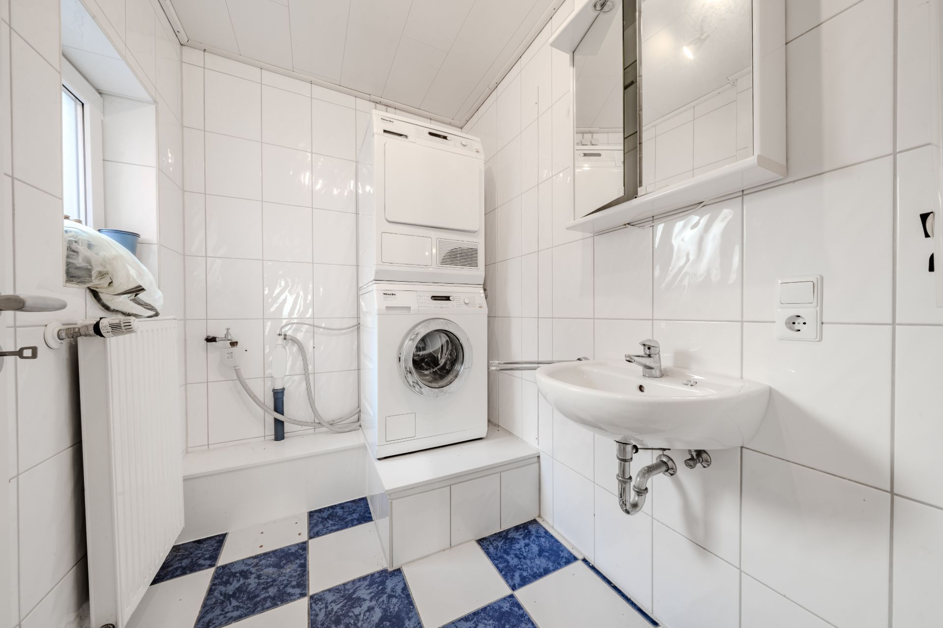 Helles Badezimmer mit Waschmaschine und Trockner, Waschbecken und kariertem Boden.