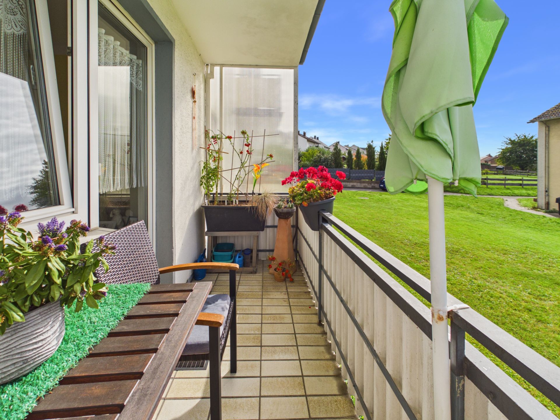 Balkon mit Tisch, Stuhl, Pflanzen und Aussicht auf einen grünen Garten.