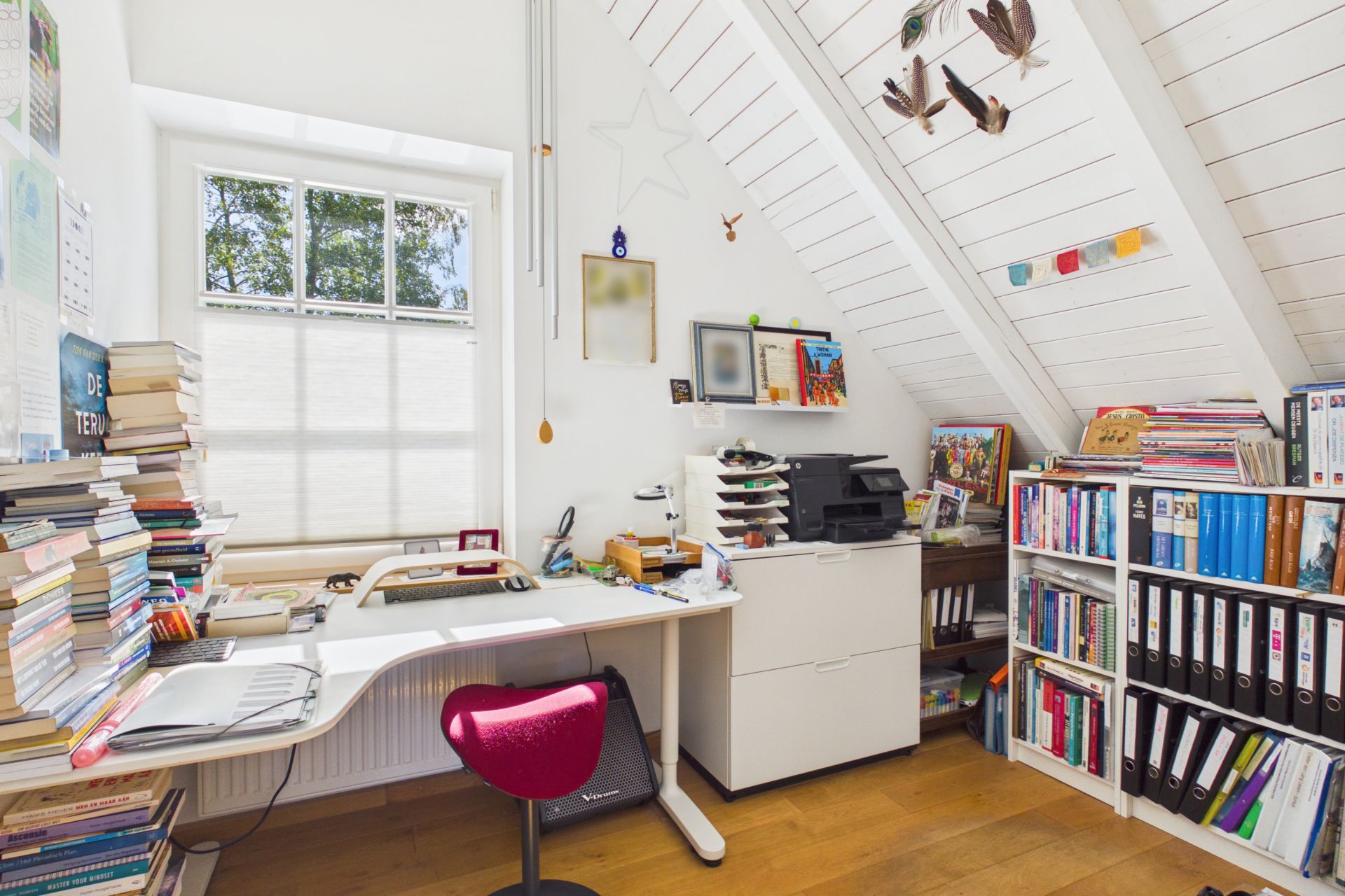 Helles Arbeitszimmer mit Schreibtisch, Stuhl, Bücherregalen und Fenster unter schrägem Dach.