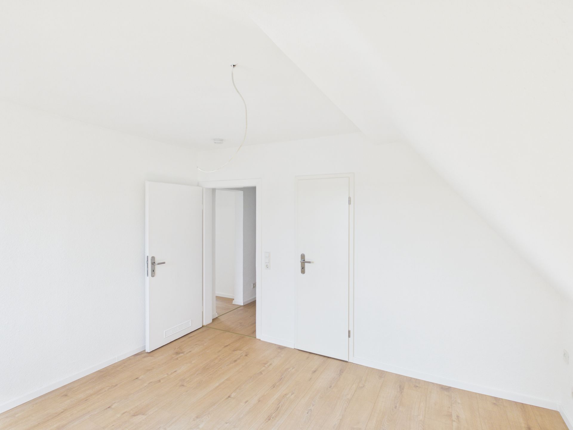 Heller leerer Raum mit weiß gestrichenen Wänden, Holzboden und zwei Türen.