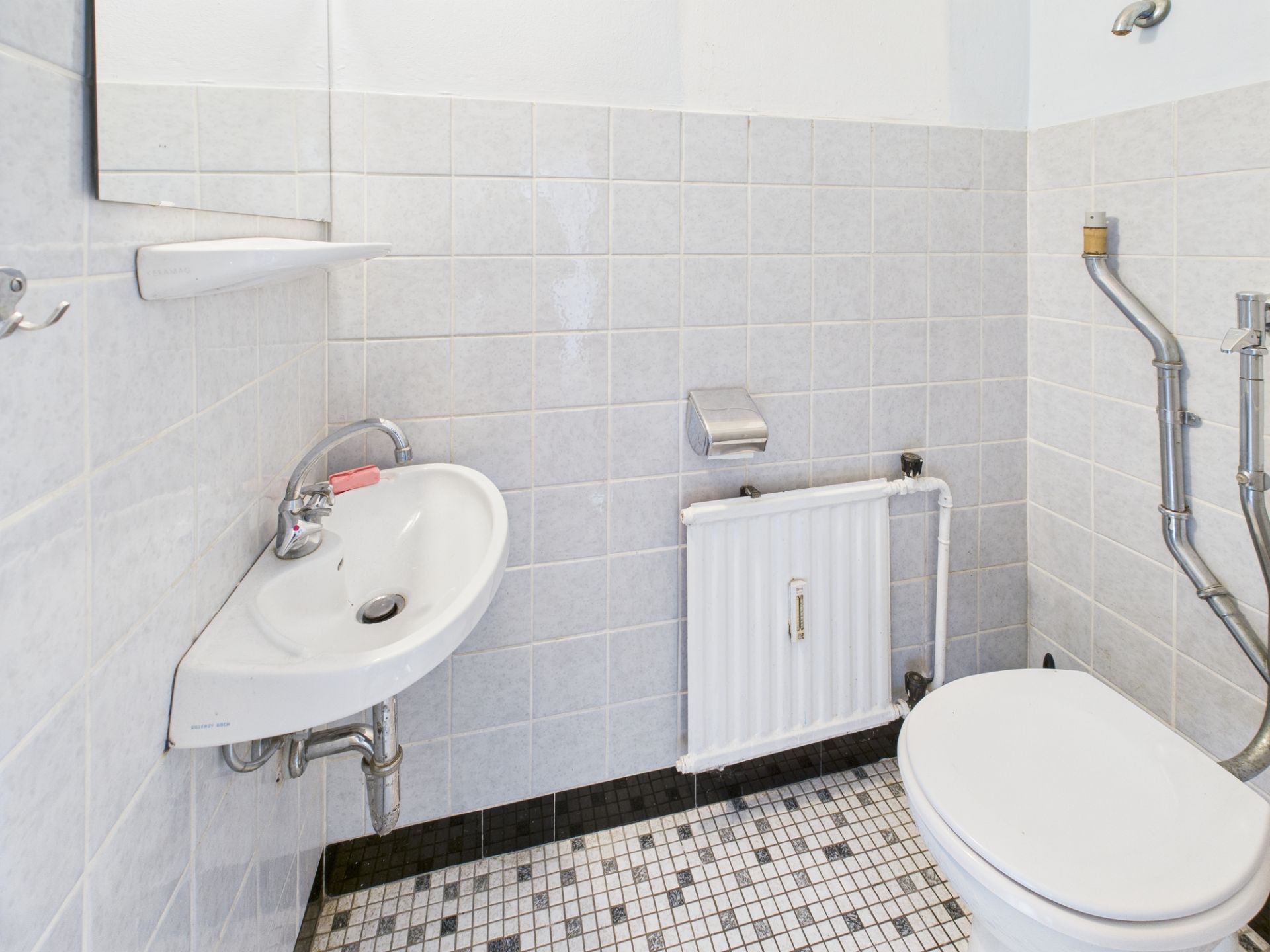 Kleines Badezimmer mit Waschbecken, Toilette, Heizung und gefliestem Boden.