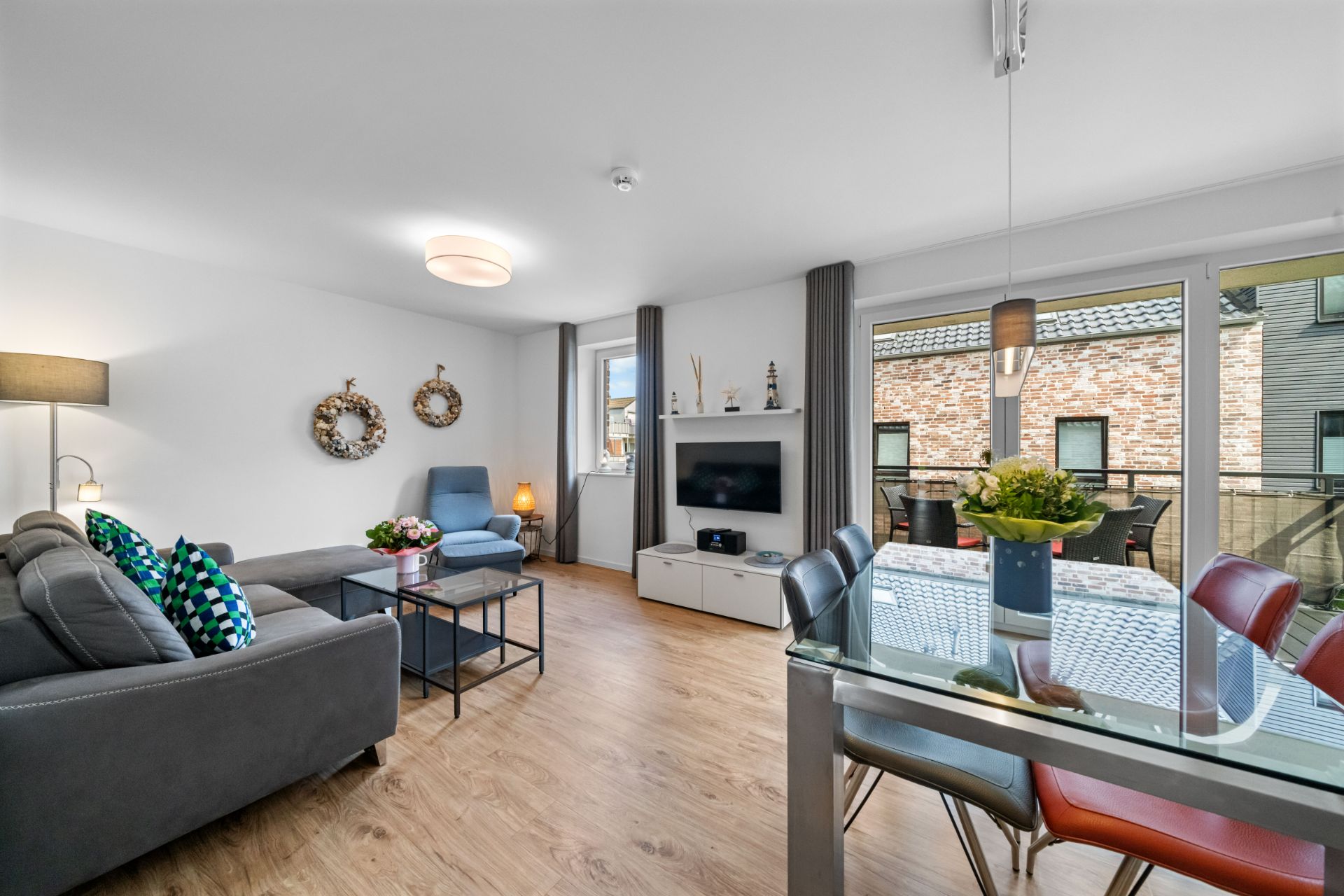 Helles Wohnzimmer mit Sofa, Sessel, Esstisch und TV, große Fenster zur Terrasse.