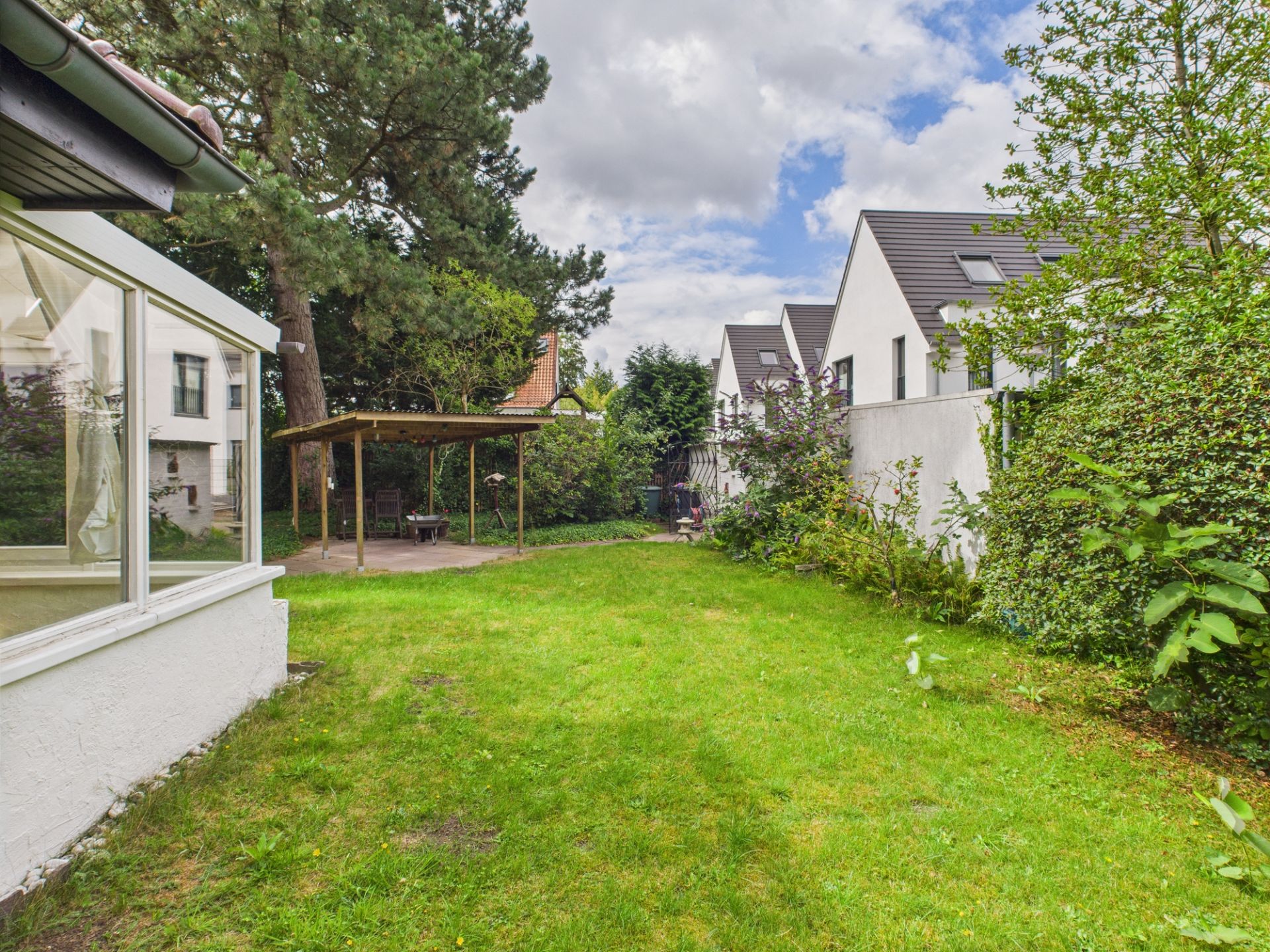 Grüner Garten mit Rasen, Begrenzung durch Hecken und Nachbarhäuser.