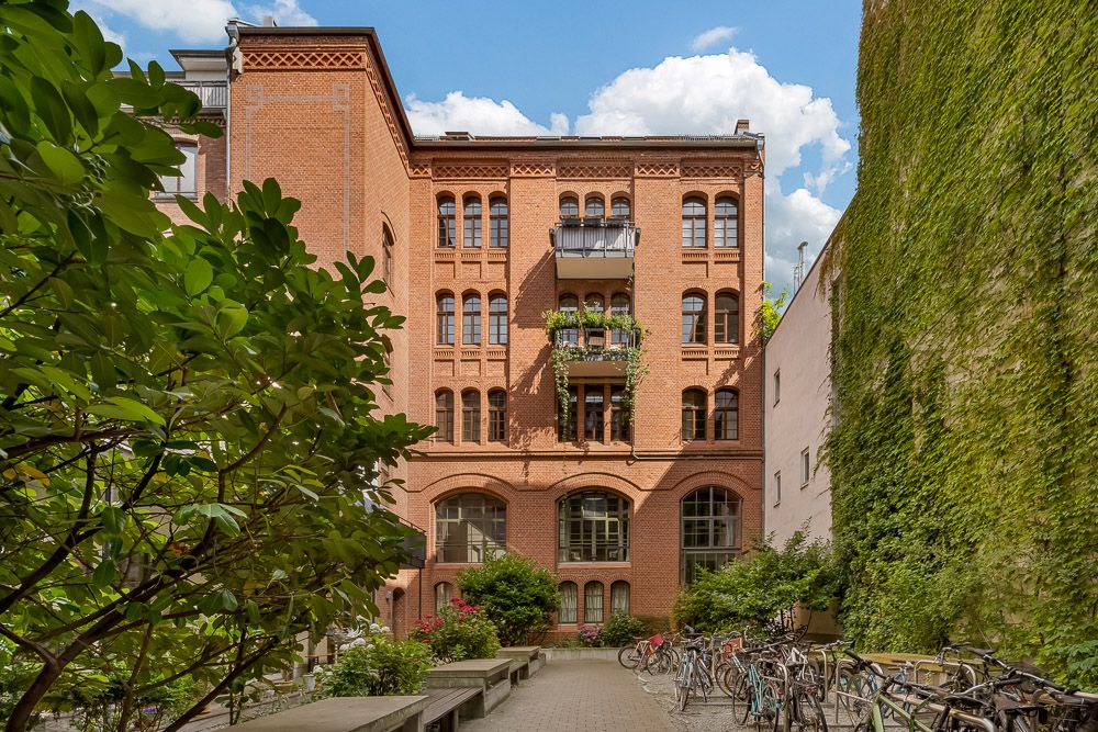 Roter Backsteinwohnhaus mit Balkonen, Pflanzen und Fahrrädern im begrünten Innenhof.