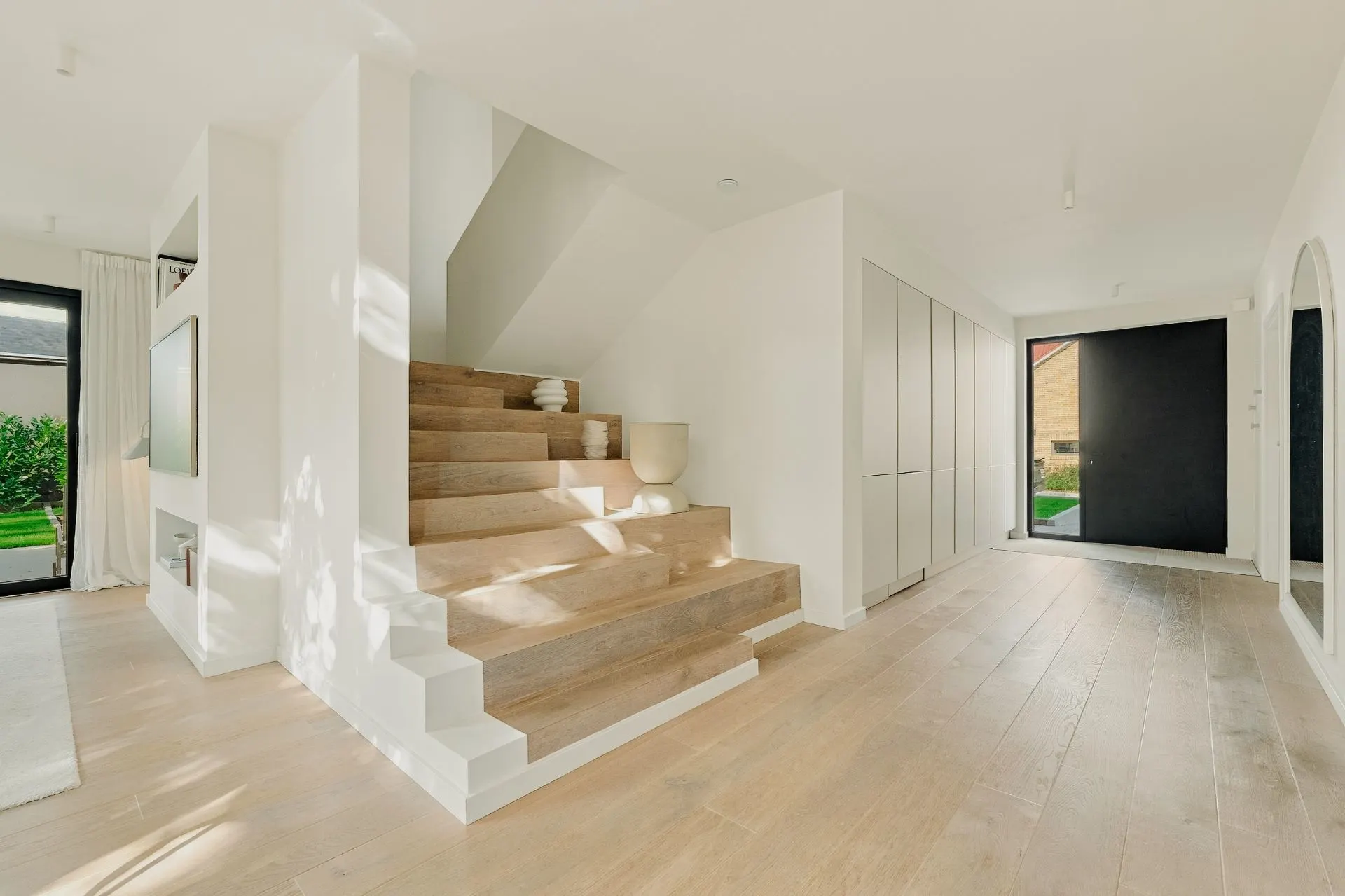 Heller Flur mit Holztreppe, großen Fenstern und Einbauschränken.