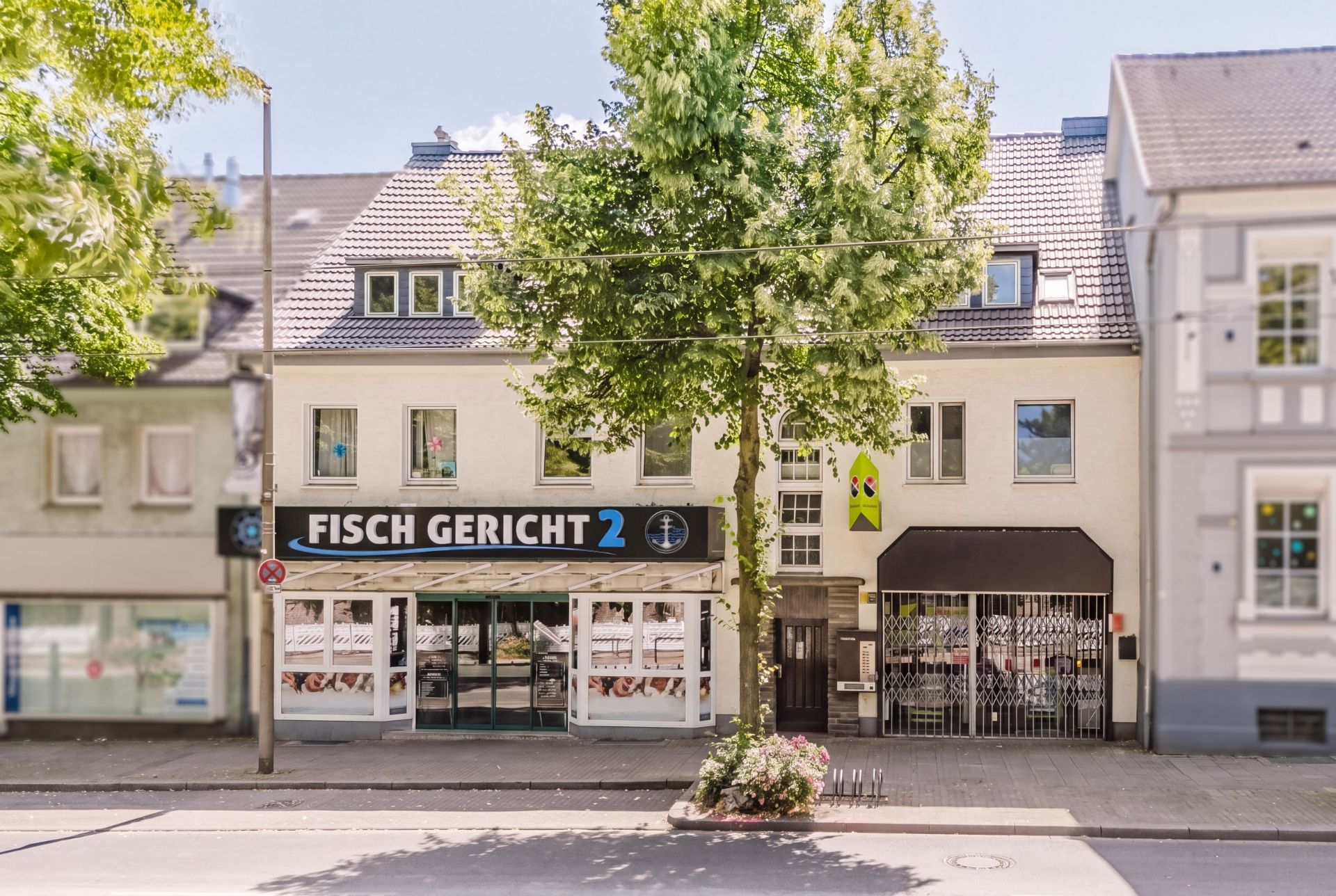 Mehrstöckiges Wohnhaus mit Geschäft im Erdgeschoss und Baum davor.