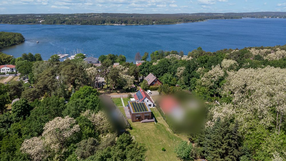 Luftaufnahme eines Hauses mit Solarpanel, umgeben von Bäumen, nahe einem großen See.