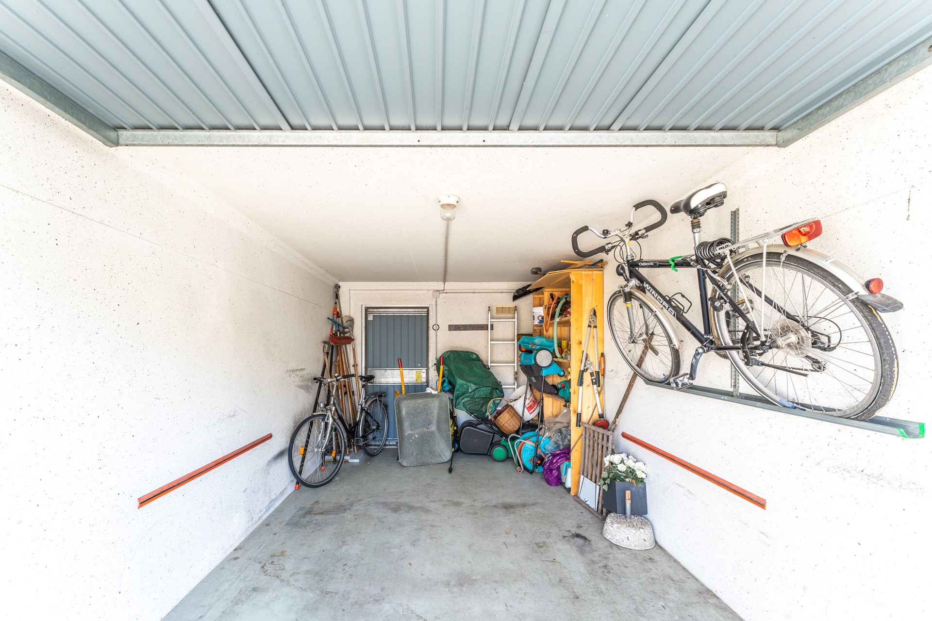 Ordentliche Garage mit Fahrrädern, Gartenwerkzeug und Regalen an den Wänden.