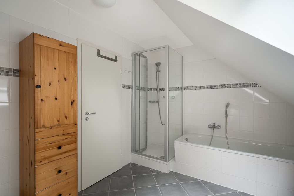 Modernes Badezimmer mit Holzschrank, Dusche und Badewanne unter einer Schräge.
