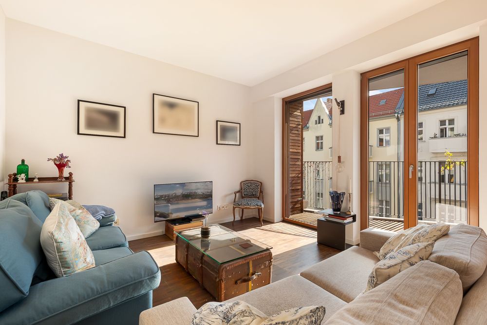Helles Wohnzimmer mit Sofa, Sessel, Couchtisch, TV und Zugang zu einem Balkon mit Glasfront.