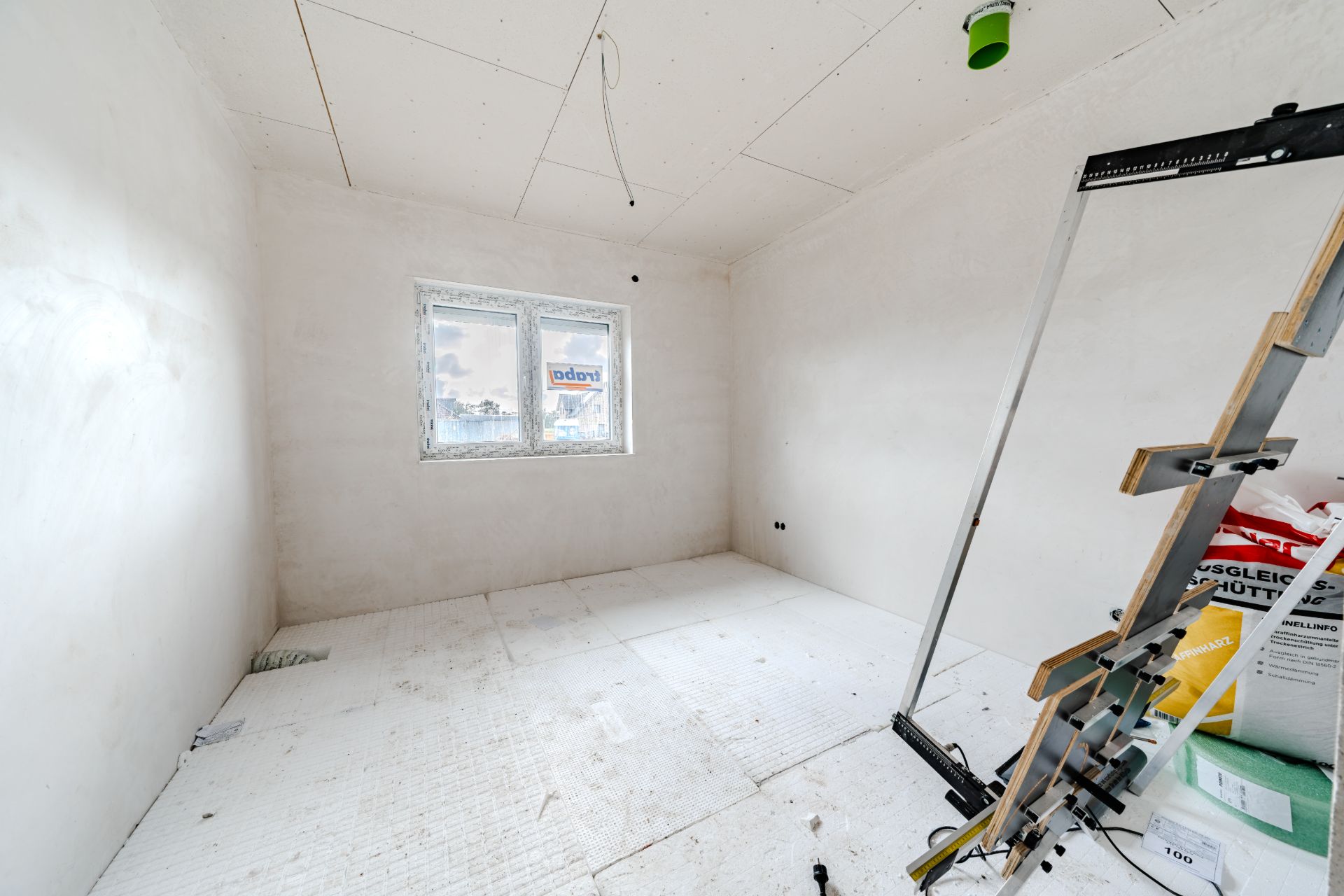 Helles, unfertiges Zimmer mit weißem Boden und einer Leiter, Fenster an der Rückwand.