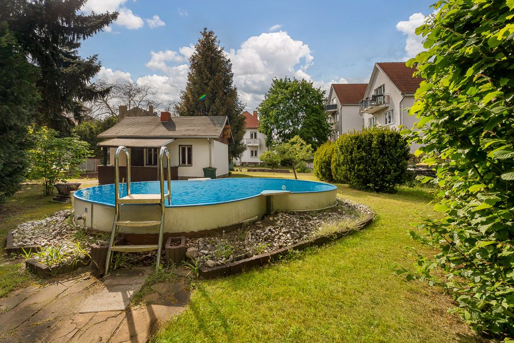 Runder Aufstellpool mit Leiter im Garten vor einem kleinen Haus.