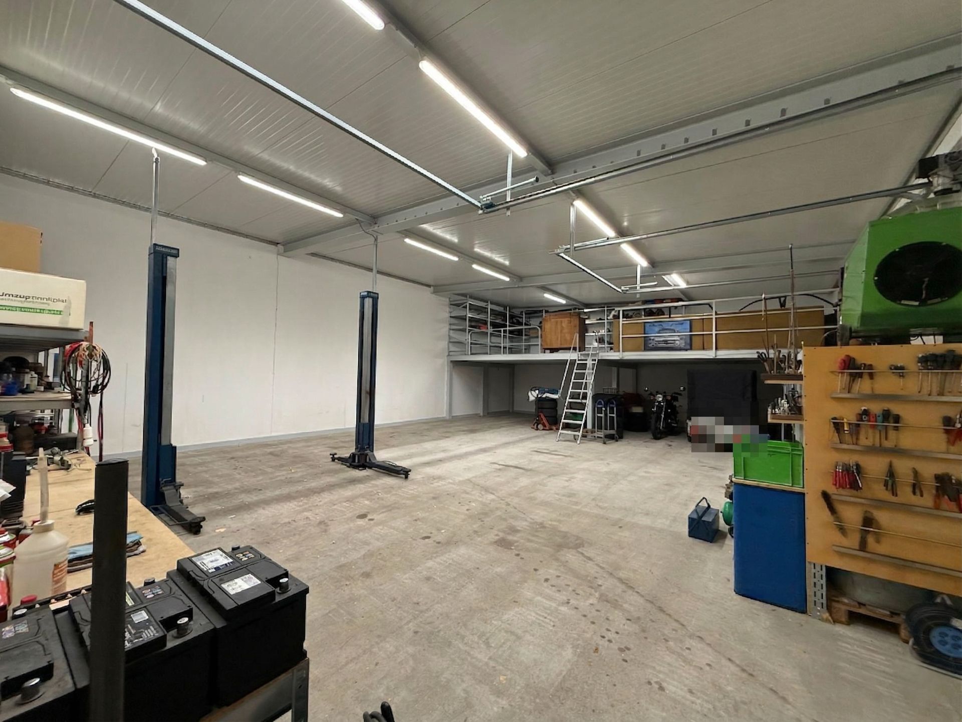 Große Garage mit Werkbänken, Werkzeugregalen, Hebebühnen und einer Empore mit Treppe.