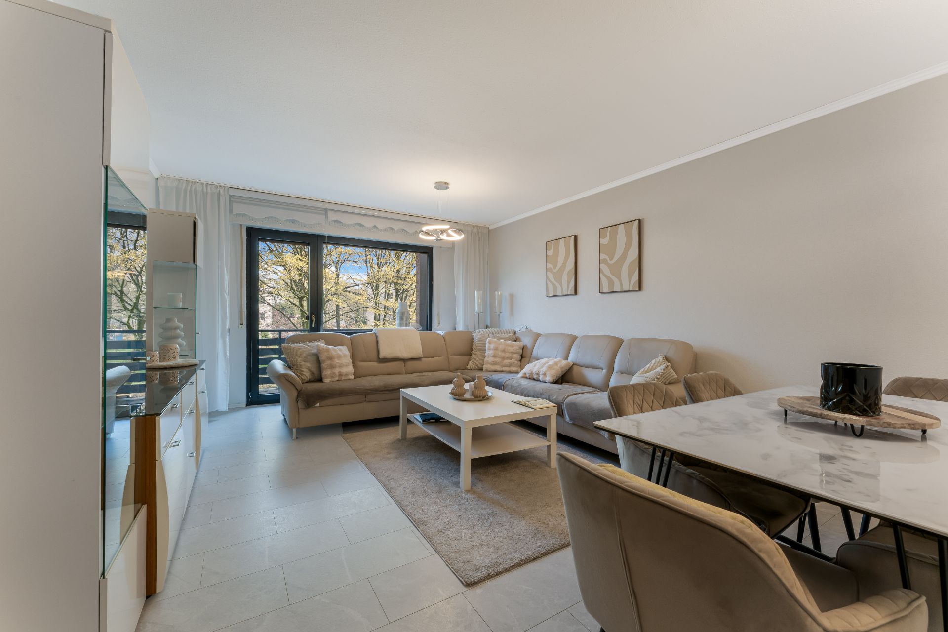 Modernes Wohnzimmer mit großer Eckcouch, Couchtisch, Esstisch und breiten Fenstern.