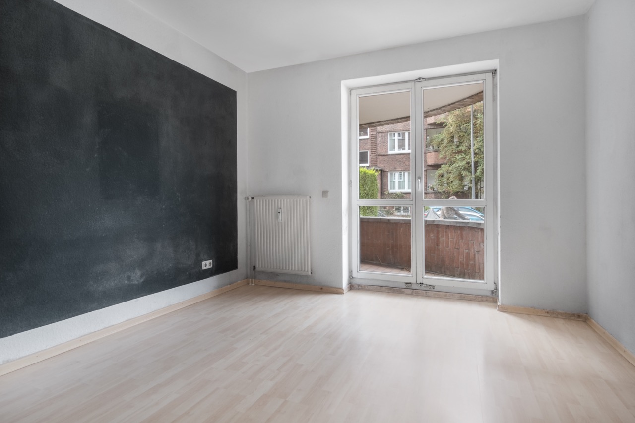 Leerer Raum mit heller Holzfußboden, dunkler Wand und großer Glastür zu einem Balkon.