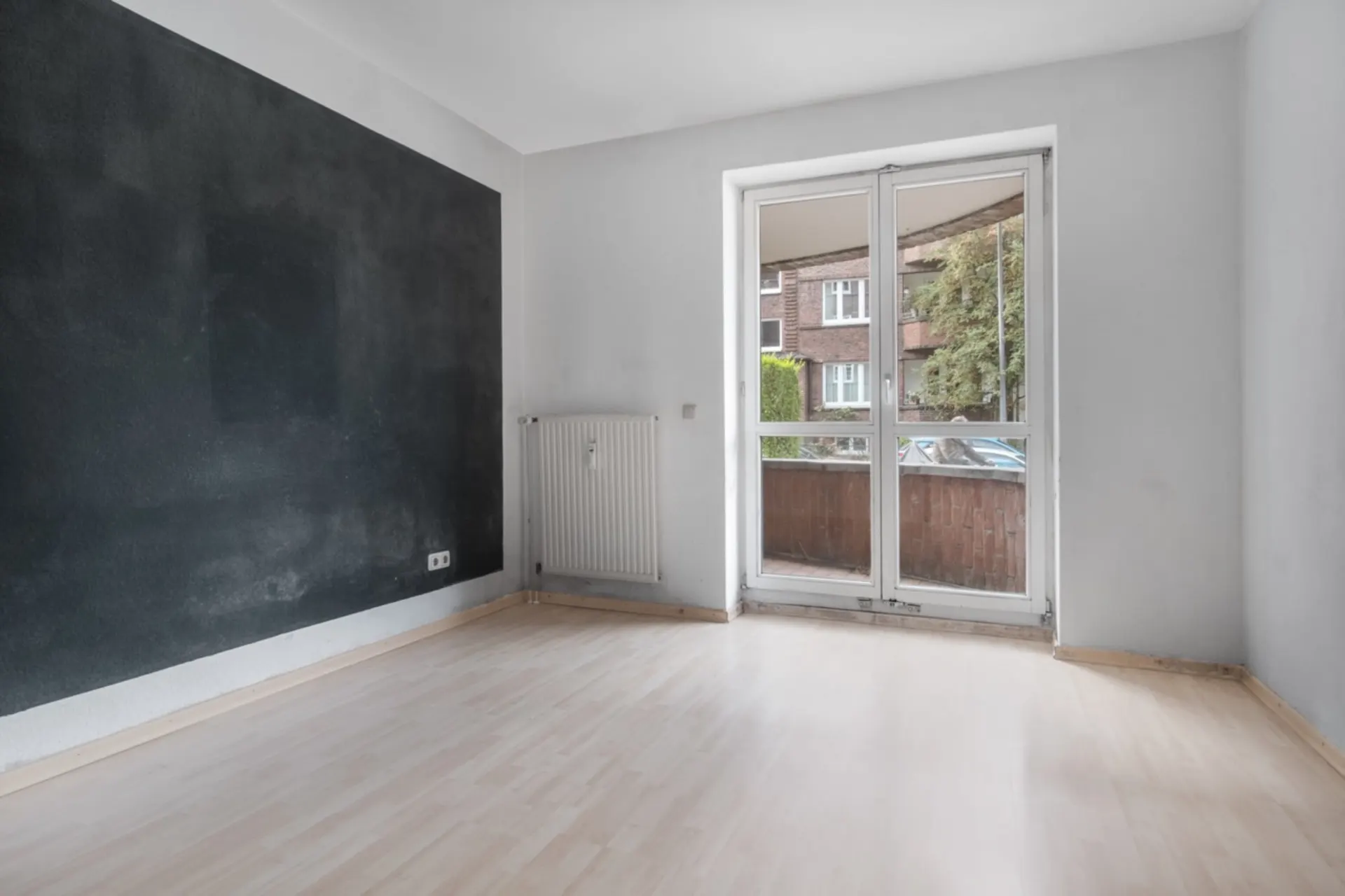 Leerer Raum mit heller Holzfußboden, dunkler Wand und großer Glastür zu einem Balkon.