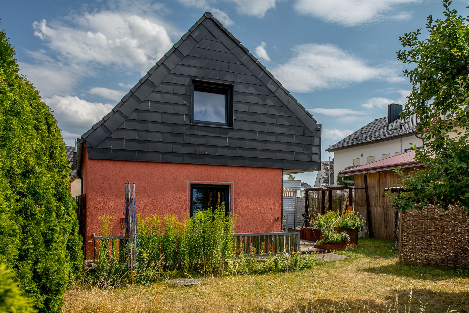 Kleines Wohnhaus mit roter Fassade, schwarzem Dach und Garten im Vordergrund.