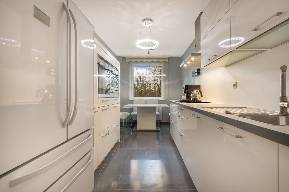 Moderne, helle Einbauküche mit Esstisch, Kühlschrank und Fenster mit Blick ins Grüne.