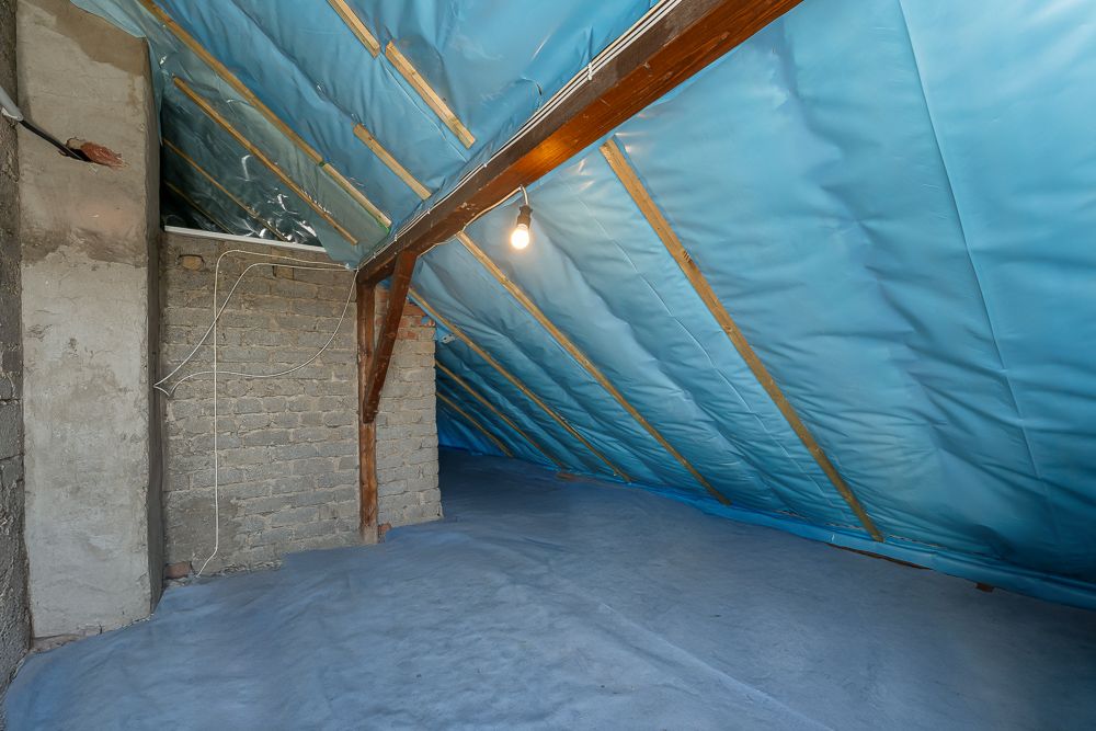 Dachboden mit blauer Folienabdeckung, Holzbalken und sichtbaren Ziegelwänden.
