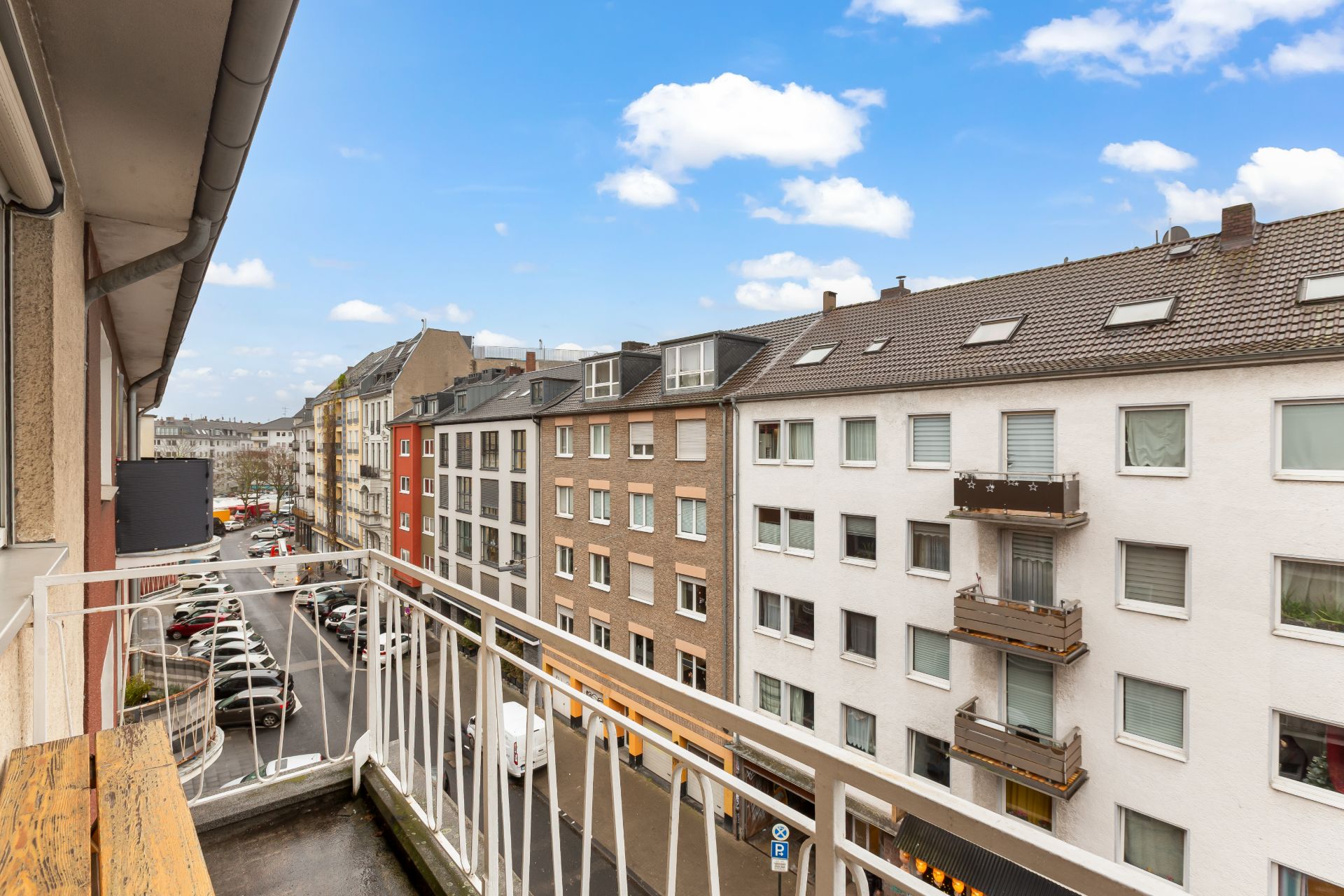 Blick von einem Balkon auf eine Stadtstraße mit mehreren Wohnhäusern.