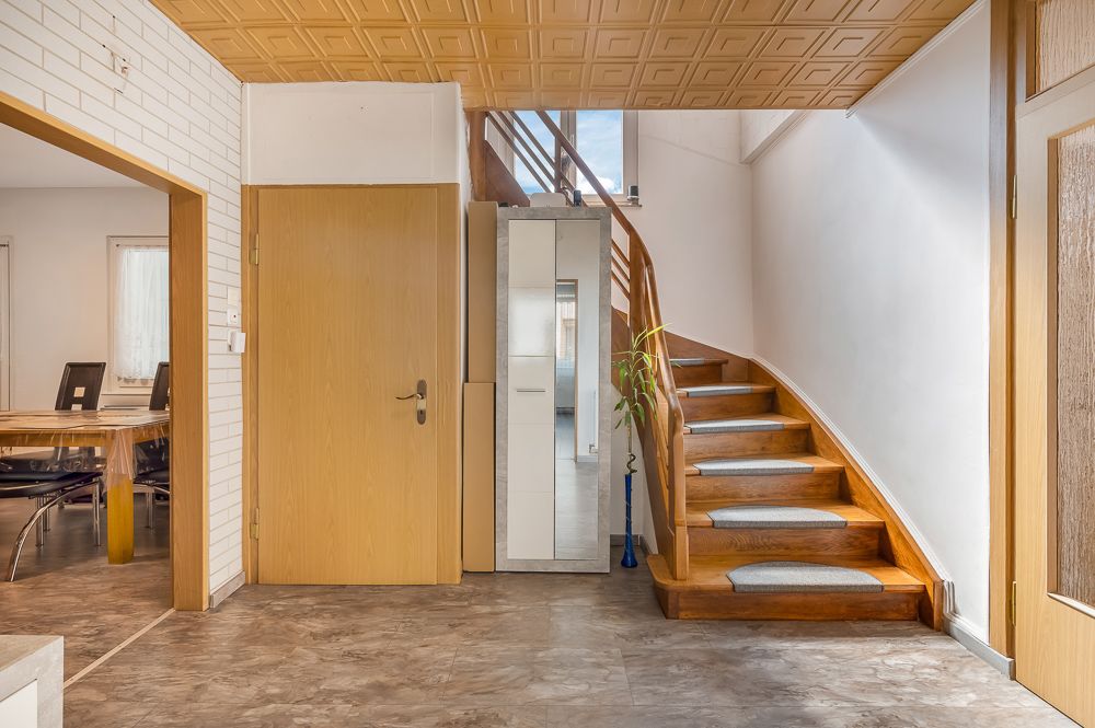 Flur mit Holztreppe, Schrank und Zugang zu einem Esszimmer mit Tisch und Stühlen.
