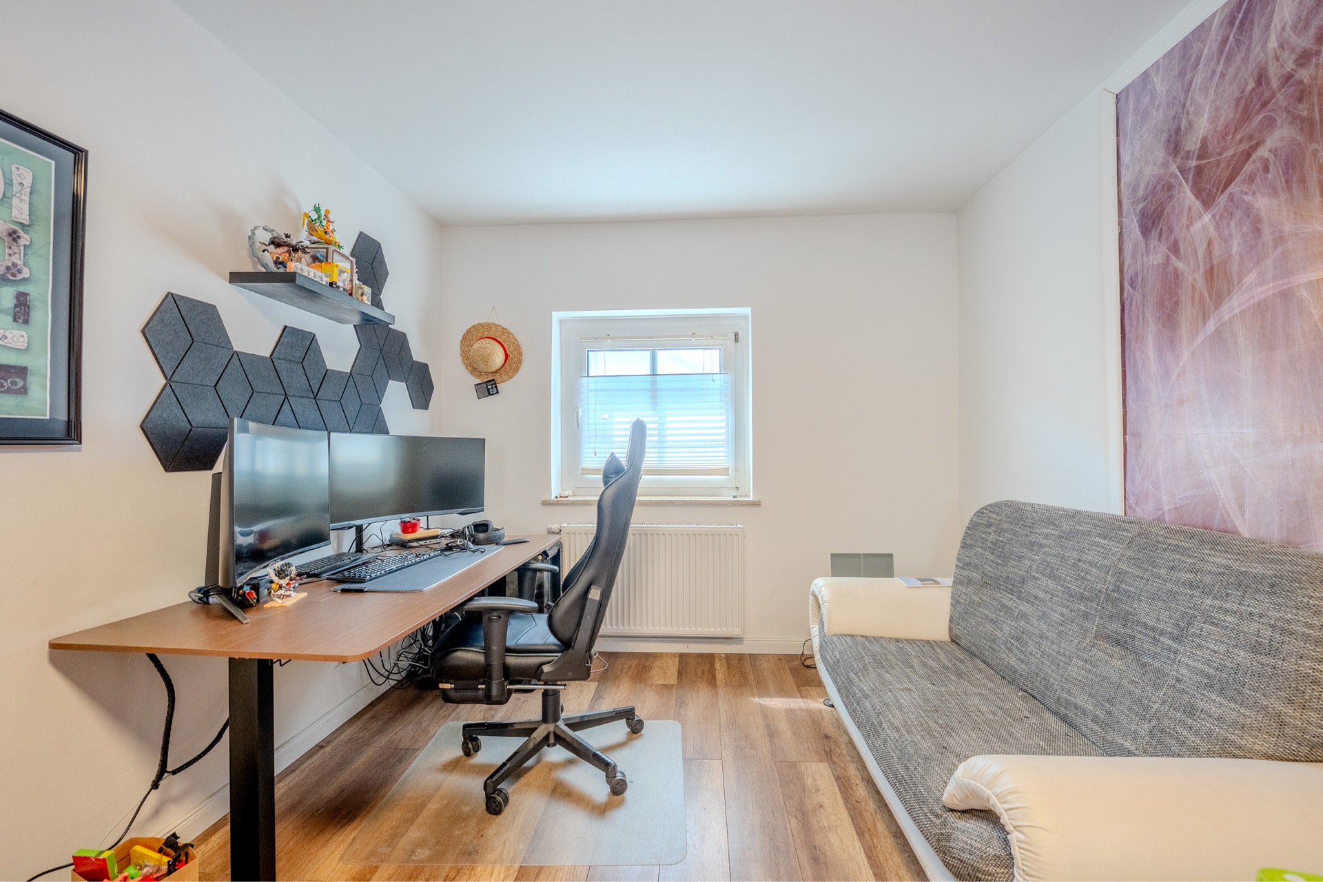 Arbeitszimmer mit Schreibtisch, zwei Monitoren, Bürostuhl und grauem Sofa.
