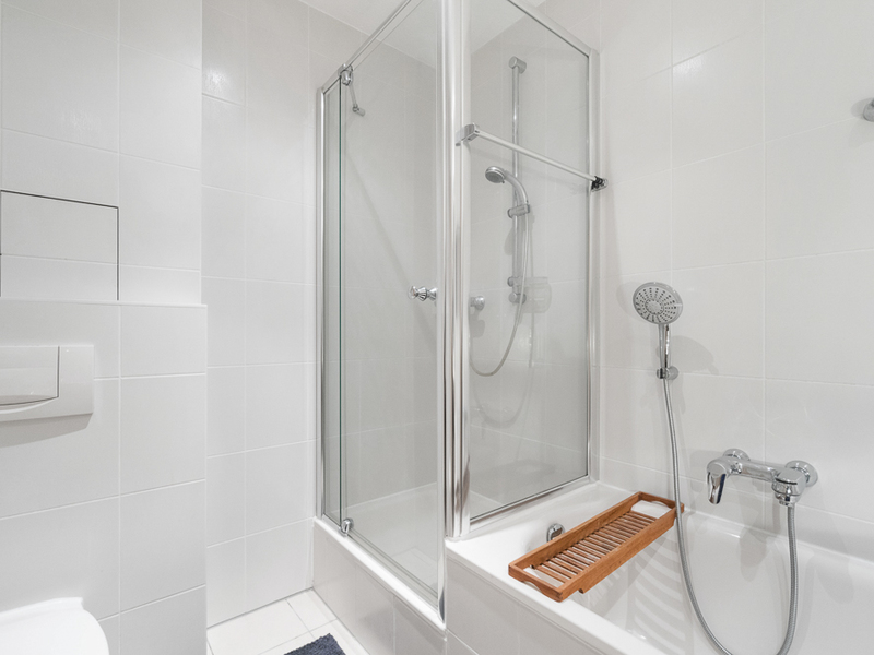 Helles Badezimmer mit Dusche, Badewanne und Holzgitter auf dem Wannenrand.