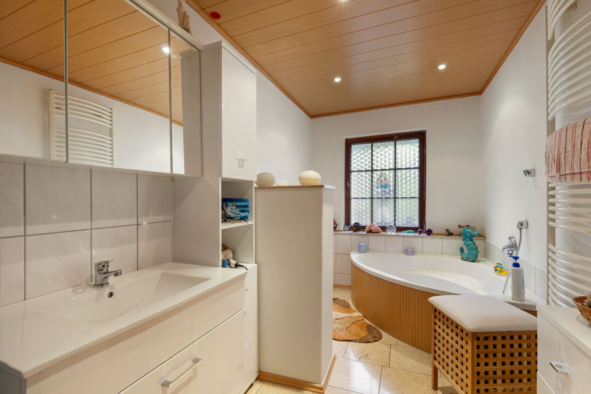 Modernes Badezimmer mit Eckbadewanne, Waschbecken, Spiegel und Holzdecke.