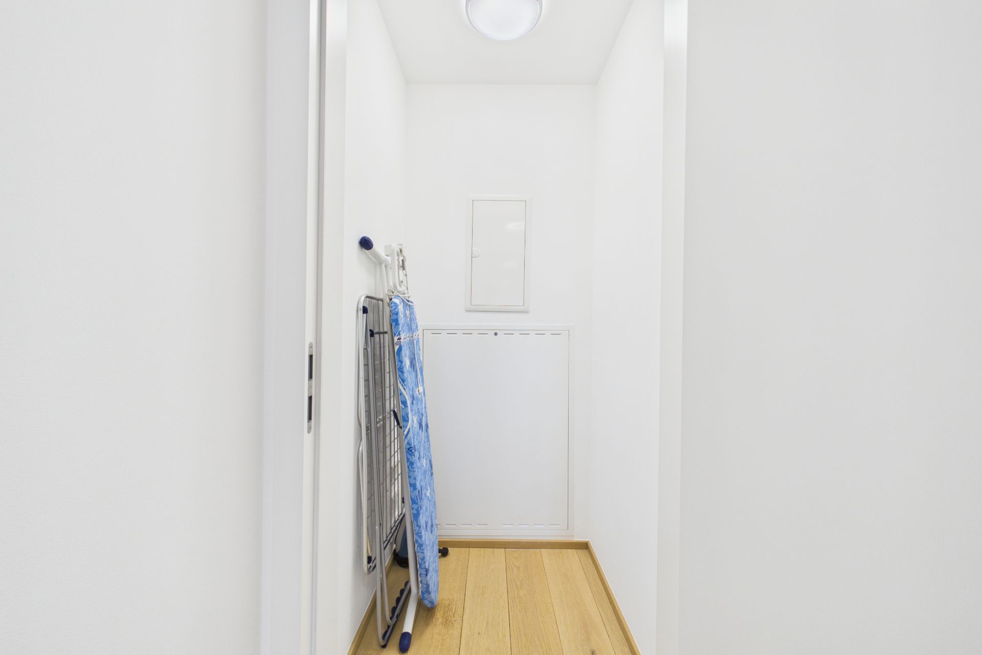 Schmaler Flur mit Parkettboden, Bügelbrett und Wäscheständer an der Wand.