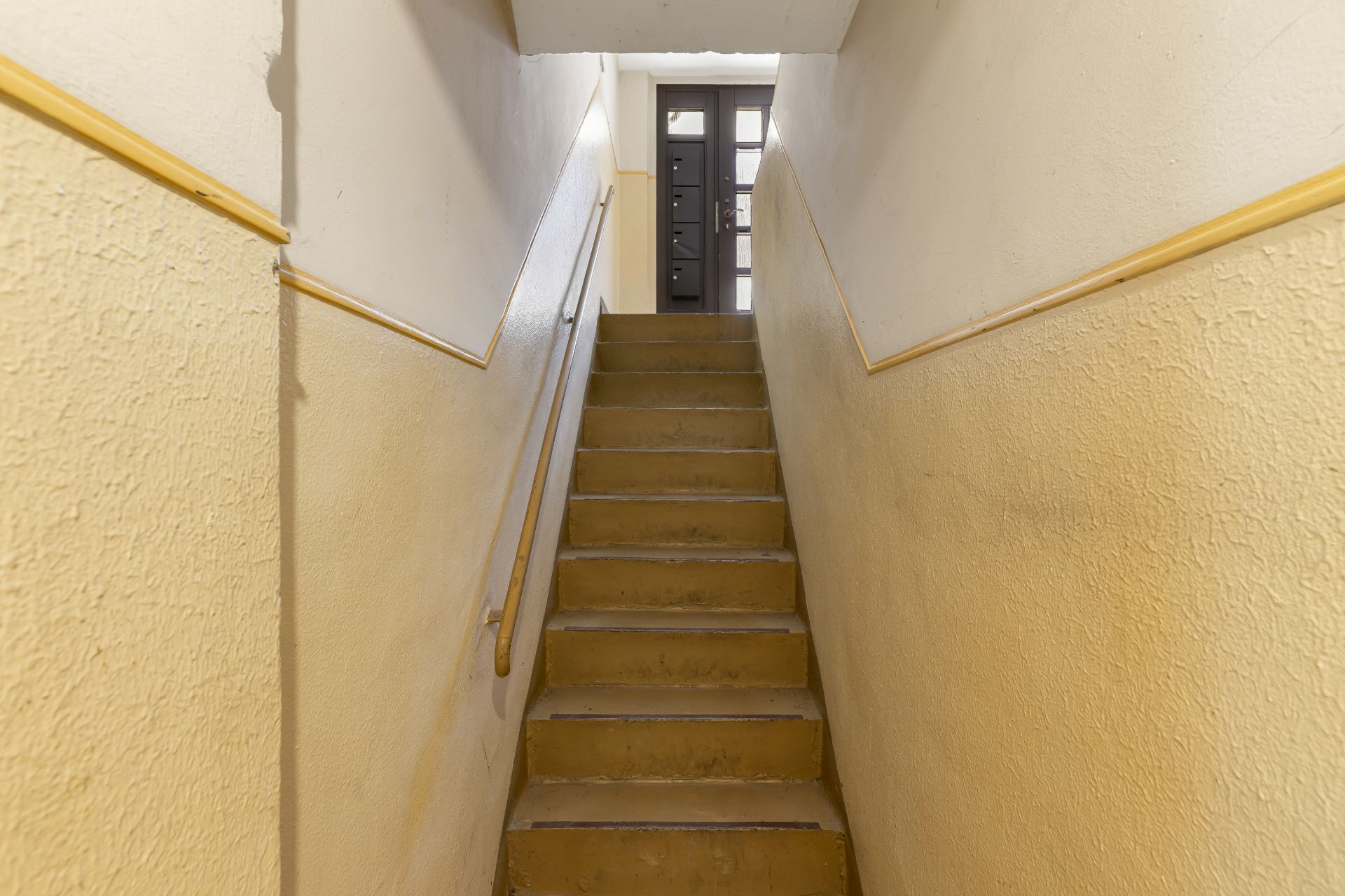 Treppe in einem Wohngebäude mit Geländer und Tür am oberen Ende.