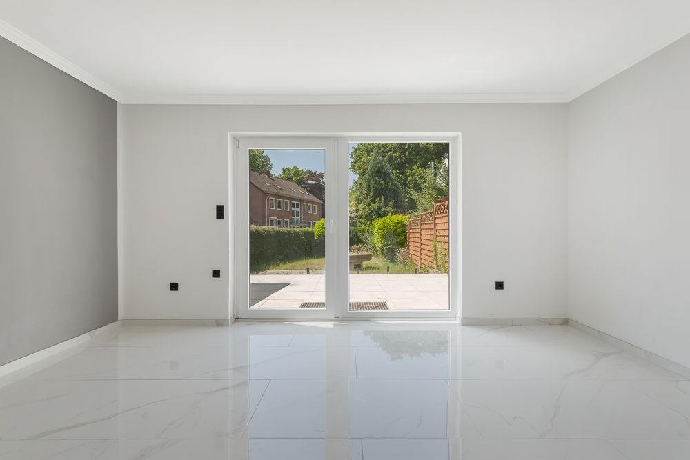 Leerer, heller Raum mit weißen Wänden, großem Fenster und Blick auf den Garten.