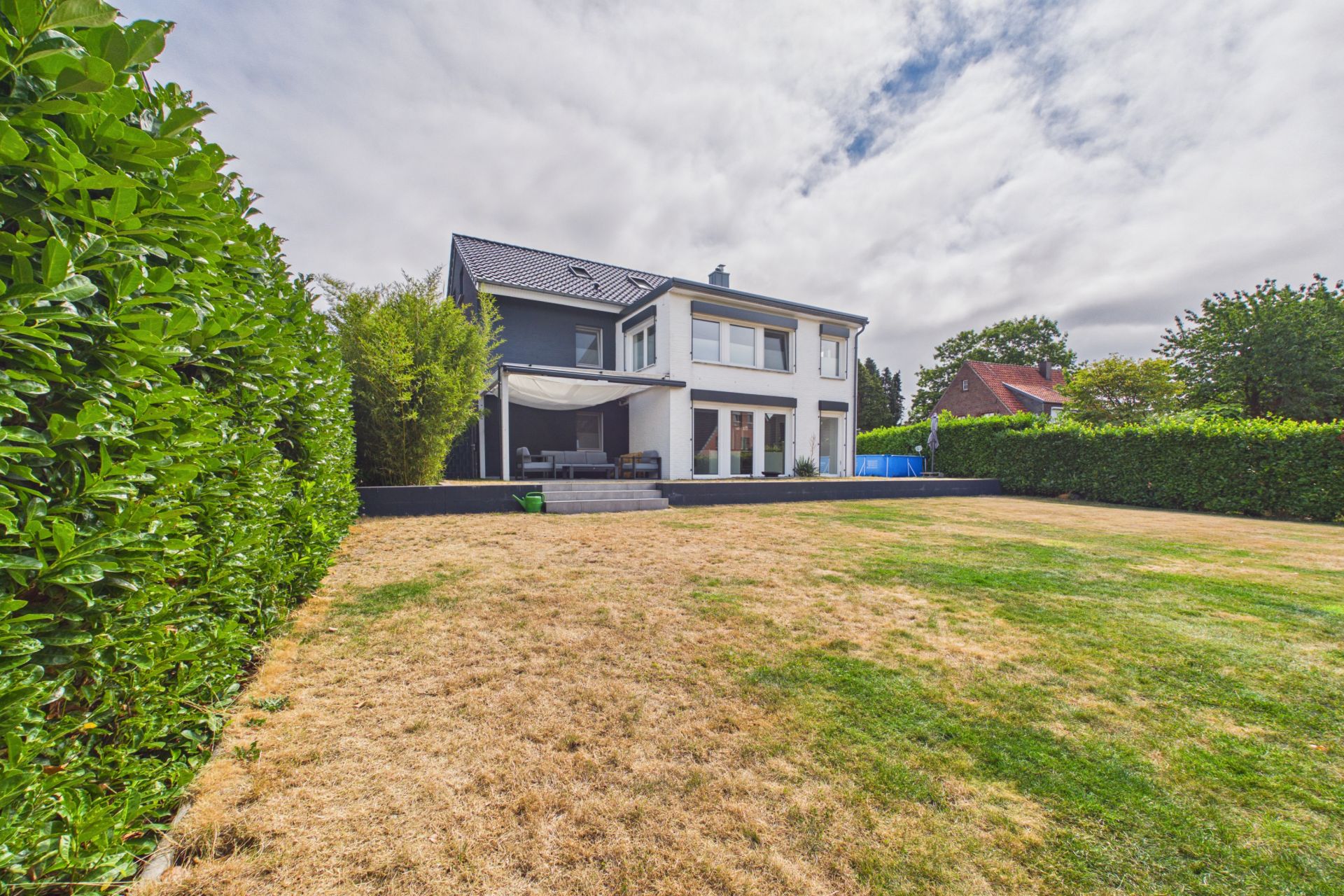Modernes zweistöckiges Haus mit Terrasse und großem Garten, umgeben von Hecken.