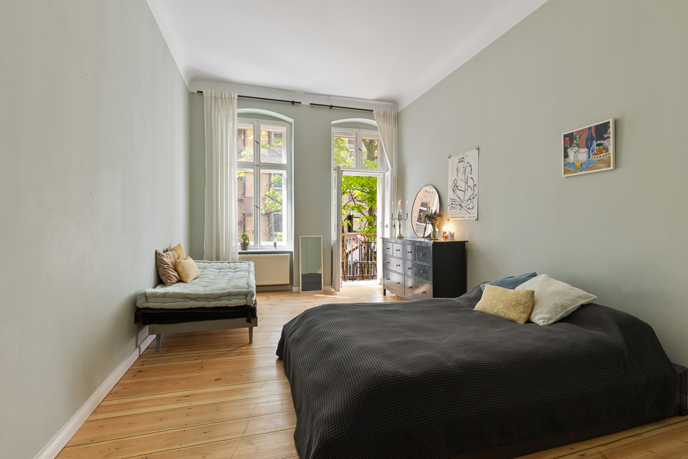 Helles Schlafzimmer mit Doppelbett, Einzelbett, Kommode und Zugang zu einem Balkon.
