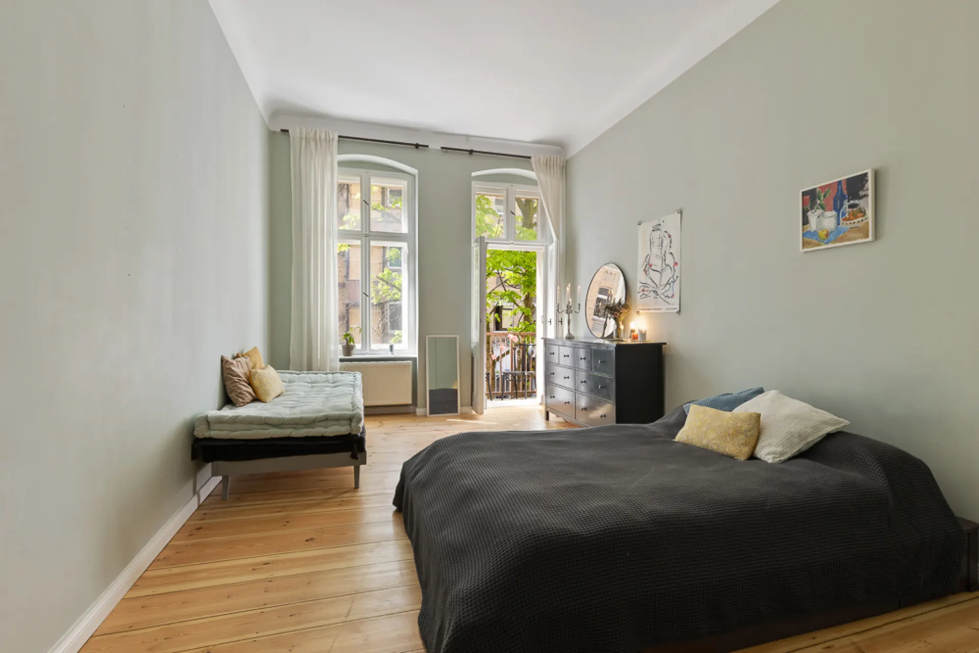 Helles Schlafzimmer mit Doppelbett, Einzelbett, Kommode und Zugang zu einem Balkon.