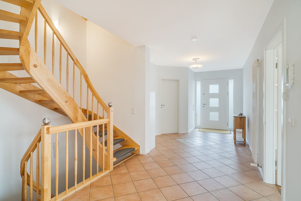 Heller Flur mit Holztreppe, gefliestem Boden und weißer Eingangstür.