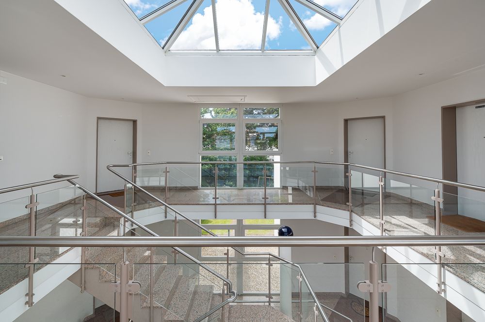 Helle Diele mit Treppe, Glasgeländer und Dachfenster, Blick auf Fenster mit Außensicht.