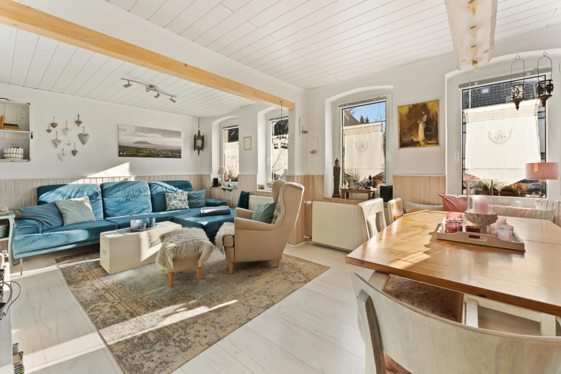 Helles Wohnzimmer mit blauem Sofa, Teppich, Essbereich und großen Fenstern.