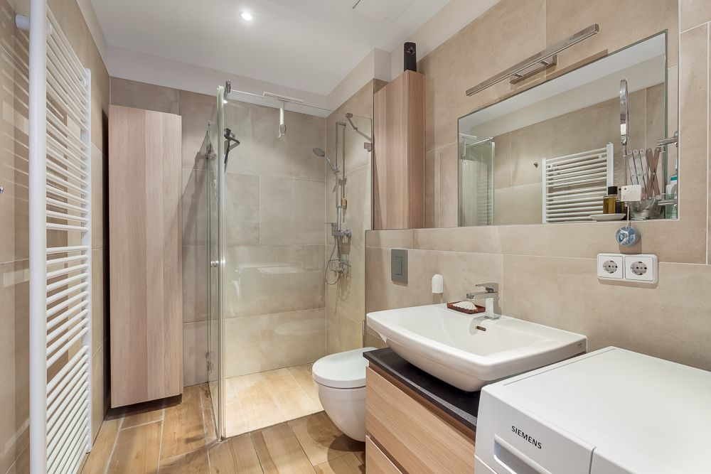 Modernes Bad mit Dusche, Waschbecken, WC, Waschmaschine und Holzschränken.