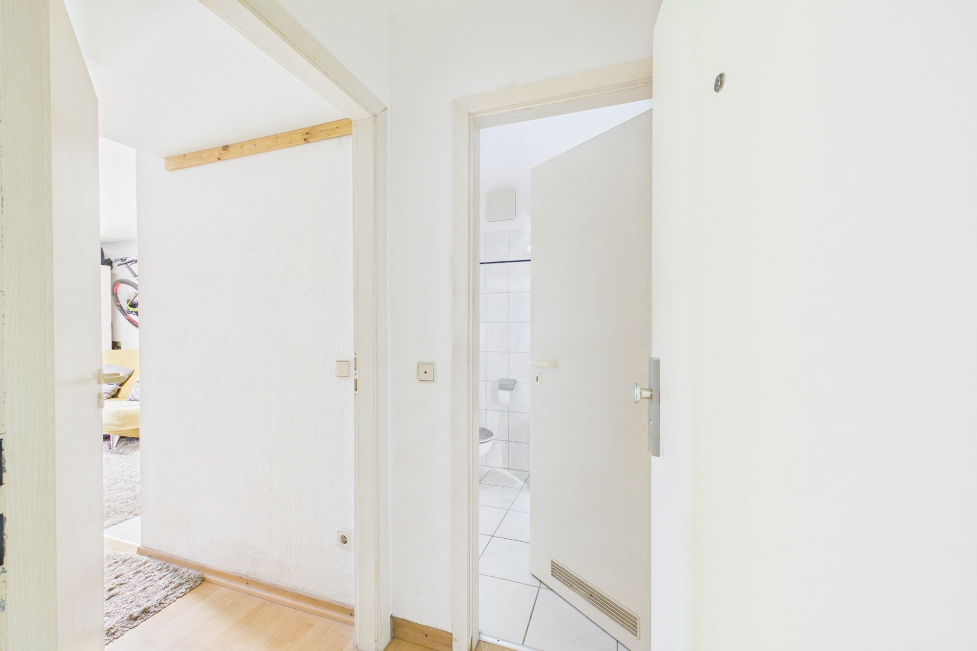 Heller Flur mit Blick in ein Badezimmer und ein Wohnzimmer mit gelbem Sofa.